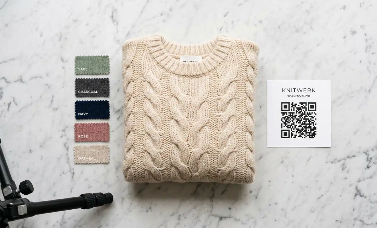 Flat lay product photography setup with a folded sweater and a printed QR code card on a marble surface.