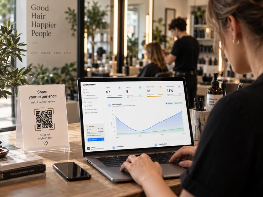 La titolare di un salone controlla dal bancone un pannello di scansioni sul portatile, accanto a un cartoncino “Share your experience” con un QR code.