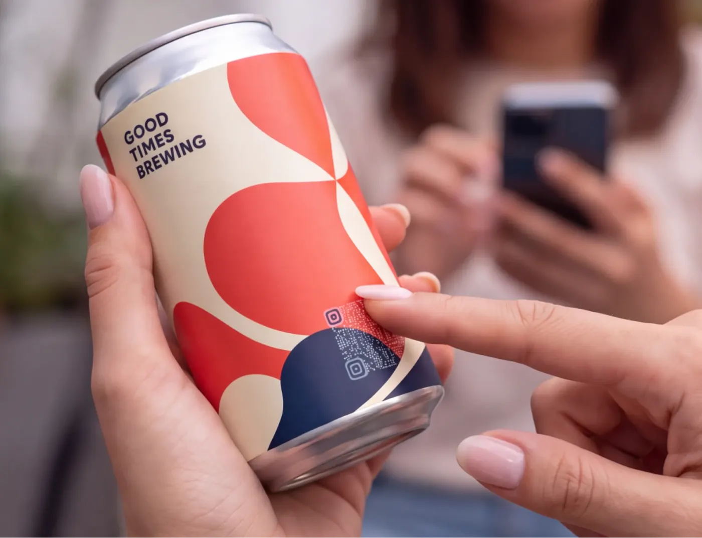 A finger points to the invisible QR code blended into a Good Times Brewing can while someone scans it in the background